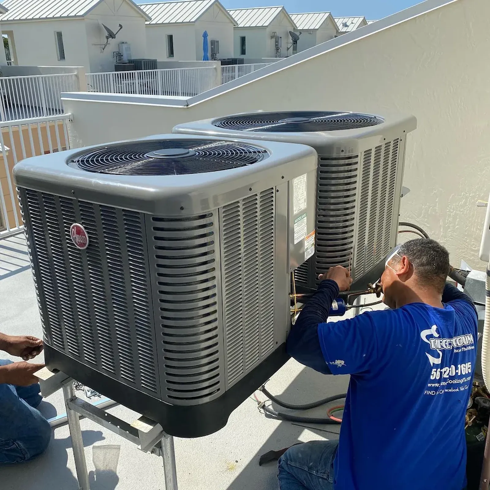 A Direct Cooling technician brazes the refrigerant connections on a pair of new Rheem condensers mounted on a raised stand. Direct Cooling technician connecting refrigerant lines on two new Rheem condensers on a raised stand